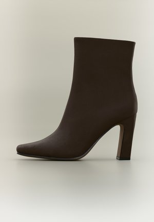 Bottine en cuir marron foncé avec bout pointu et talon bloc haut sur fond neutre.