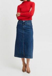 Midi skirt denim dengan potongan lurus, warna biru, dan belahan depan. Dipasangkan dengan atasan lengan panjang merah dan sepatu hak tinggi cokelat.