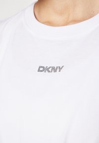 Balta kokvilnas T-kreklu ar rhinestone akcentu logo "DKNY" uz krūtīm, klasiskām apļveida kakla izgriezumu un gludu tekstūru.