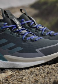 Herren Wanderschuhe, oberer Teil in dunkelgrau mit Netztextur, blaue Schnürsenkel, hellgraue Akzente und gepolsterte weiße Sohle. Verfügt über eine Schlaufe für leichtes Anziehen.