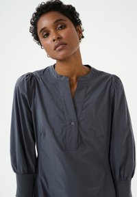 Hallitusvärviline särk nööpide ja 3/4 puffvarrukatega. Omab pehmet tekstuuri ja minimaalset kujundust.