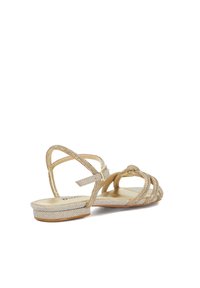 Gold strappy sandals with a bejeweled design, a flat sole, and adjustable ankle strap; features multiple crisscrossed straps.