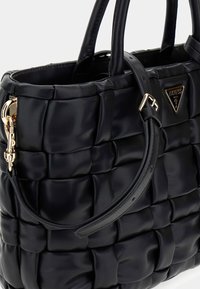 Bolso de cuero negro con un diseño acolchado, herrajes dorados y un logotipo triangular. Cuenta con dos asas y una correa desmontable.