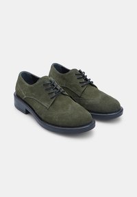 Pantofi din suede verde cu șireturi, cu o textură netedă, vârf rotund și talpă închisă. Cusături decorative pe laturi și elemente de design clasice.