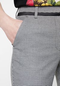Svartvita houndstooth-byxor med en slät textur, sidofickor och ett tunt svart bälte i midjan.