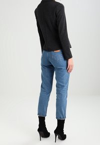 Veste noire ajustée avec un col, paire de jeans taille haute bleu clair, et bottines à talons aiguilles noires. Texture lisse et coupe ajustée.
