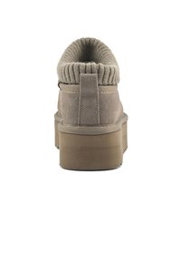 Beige mockabootie med ribbad stickad krage, tjock platåsula och förstärkt hälflik för enkel användning.