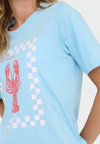 Lichtblauw katoenen T-shirt met een roze kreeft grafiek. Een dambordpatroon omlijst het ontwerp, met een ronde halslijn en korte mouwen.