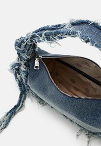 Denim torba z raztrgano teksturo, z zadrgo in zvitim ročajem. Notranjost ima svetlo podložitev s patternom logotipa. Modra barva je prisotna povsod.