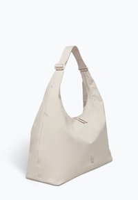 Sac à épaule beige avec une forme arrondie, fabriqué en tissu doux. Doté d'une ouverture zippée et d'une large sangle réglable. Détail de logo simple.