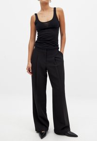 Juodas maikutė be rankovių su apvaliu kaklu ir prigludusia siluetu, derinama su juodomis platėjančiomis kelnių, aukštu juosmeniu, su priekiniais raukšlėmis.