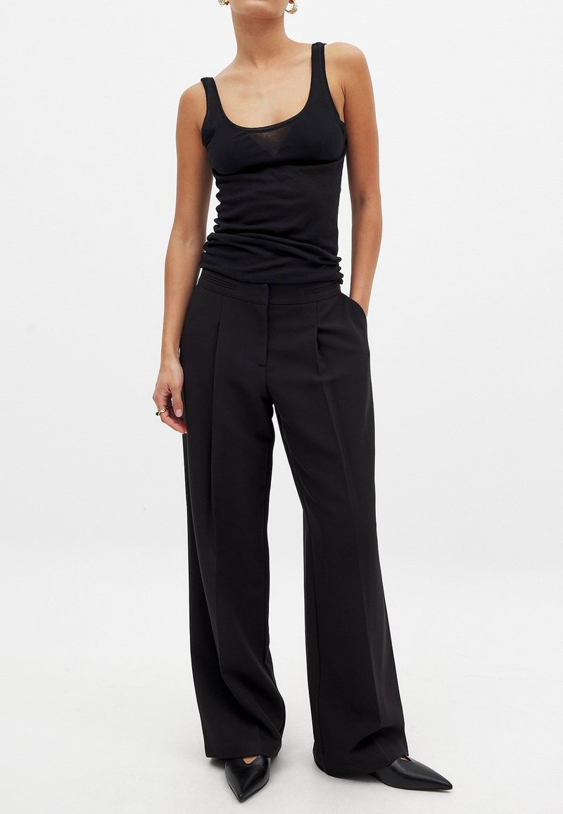 Juodas maikutė be rankovių su apvaliu kaklu ir prigludusia siluetu, derinama su juodomis platėjančiomis kelnių, aukštu juosmeniu, su priekiniais raukšlėmis.