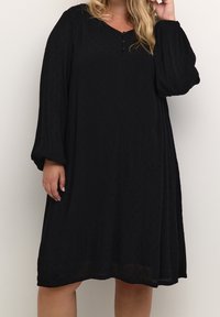 Une robe noire en tissu léger, avec des manches longues, un décolleté en V, et trois boutons décoratifs à l'avant ; surface texturée.