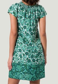 Robe à imprimé floral avec des couleurs vertes et blanches, manches courtes, encolure smockée et design en couches, présente un tissu texturé avec des motifs variés.