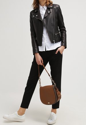 Giubbotto da motociclista in pelle nera con zip argentate, camicia bianca con colletto, pantaloni neri, borsa a tracolla marrone e sneakers bianche.