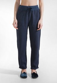 Granatowe lniane spodnie z elastycznym pasem na sznurek, dwoma przednimi kieszeniami i podwiniętymi nogawkami. W połączeniu z ciemnoniebieskimi płaskimi butami.