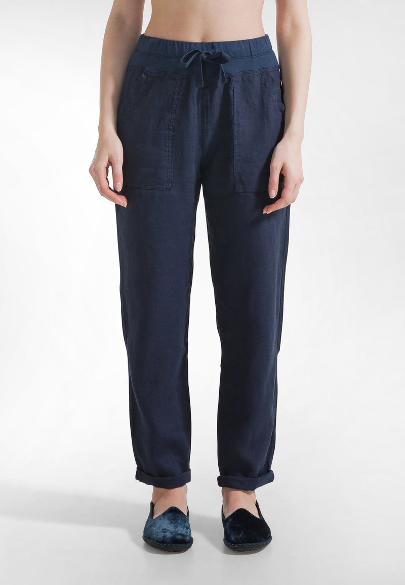 Granatowe lniane spodnie z elastycznym pasem na sznurek, dwoma przednimi kieszeniami i podwiniętymi nogawkami. W połączeniu z ciemnoniebieskimi płaskimi butami.