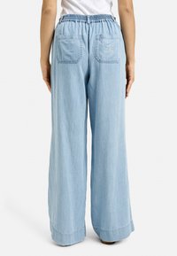 Light blue, wide-leg pants made of lightweight denim, featuring an elastic waistband and two back pockets with stitching details.