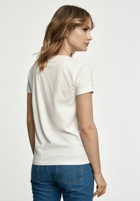 Biała bawełniana koszulka z krótkimi, podwiniętymi rękawami, dopasowany krój i okrągły dekolt. Noszona z niebieskimi dżinsami, prezentując prosty, casualowy styl.