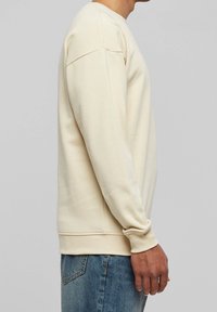 Felpa color crema con maniche lunghe, polsini e orlo a costine. Texture liscia e vestibilità comoda, progettata per il comfort e la libertà di movimento.