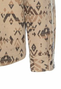 Beige langekous stof shirt met een geometrisch bruin en zwart patroon, voorzien van een knoopsmanchet en een soepele textuur.