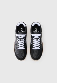 Chaussures de sport noires avec une tige synthétique texturée, des lacets blancs et une semelle en caoutchouc. Présente des détails perforés et un logo sur la languette.