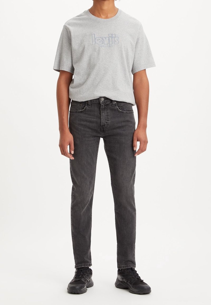 Grå bomulls-t-shirt med blå Levi's-logotyp, kombinerad med svarta jeans. Jeansen har en smal passform och klassisk femficksdesign. Svarta sneakers kompletterar looken.