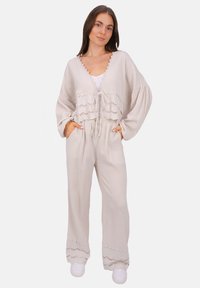 Helles beige, zweiteiliges Outfit mit einem strukturierten, offenen Oberteil mit Spitze und passenden, weit geschnittenen Hosen mit gewellten Akzenten.