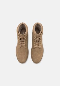 Stivaletti alla caviglia in suede marrone con punta tonda, cuciture in rilievo e lacci coordinati. All'interno, fodera morbida e suola in gomma flessibile.