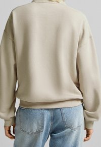 Beige sweatshirt med ribbstickade mudd och nederkant, har en avslappnad passform och mjuk textur. Kombinerad med ljusblå högmidjade jeans.