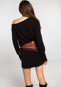 Vestido de suéter negro con escote off-shoulder, con puños y dobladillo acanalados. Cintura adornada con una bufanda burgundy estampada, con acentos dorados.