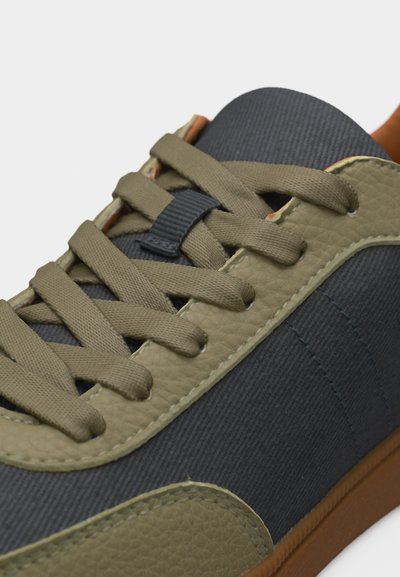 Κοντινό πλάνο αθλητικού παπουτσιού με κορδόνια και περιθώριο σε ελιά πράσινο, επάνω μέρος από σκούρο ύφασμα και καφέ σόλα.