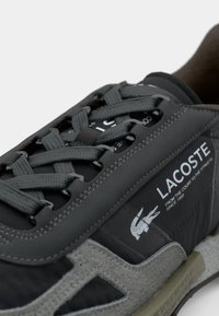 Lacoste sneakers met een grijze suede en nylon ontwerp, getextureerde veters en een merklabel. Opvallende logo-accenten aan de zijkant.