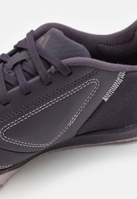 Zapatilla deportiva morada con materiales de cuero y textil, costuras en contraste y un diseño de punta redonda con suela texturizada.