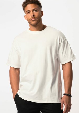 T-shirt en coton blanc avec un col rond et des manches courtes, présentant une coupe décontractée et une texture lisse, porté avec un pantalon noir.
