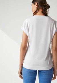 Witte T-shirt met korte mouwen, gemaakt van een gladde stof en met een afgeronde zoom. Gecombineerd met blauwe denim broek voor een casual en comfortabele uitstraling.