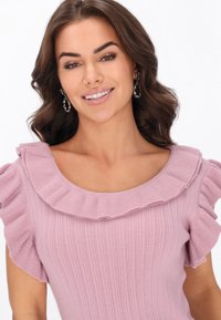 Lys pink ribbet top med korte flæseærmer og en bred udskæring ved halsen. Glat tekstur med fremhævet flæsedetalje omkring halsudskæringen.