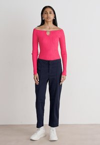 Top aderente a spalle scoperte in rosa brillante; abbinato a un pantalone navy su misura e scarpe da ginnastica bianche. Silhouette semplice e moderna.