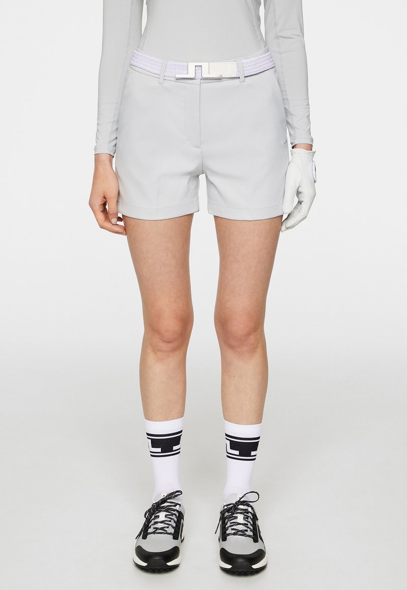 Ljust grå golfshorts med en slät textur, vikta nederkanter och framfickor. Kombinerad med ett vitt bälte och svarta och vita träningsstrumpor.