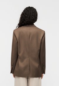 Καφέ ραμμένο σακάκι με γιακά με εγκοπές, μανίκια με ένα κουμπί και λείο υφή φινίρισμα. Το πίσω μέρος διαθέτει κεντρική ραφή.