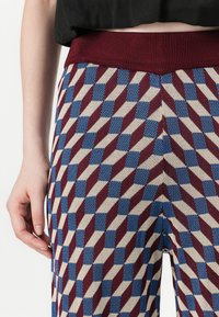 Pantaloni lavorati a maglia con un motivo geometrico di diamanti borgogna, blu e crema, dotati di una vita a coste borgogna e una finitura testurizzata.