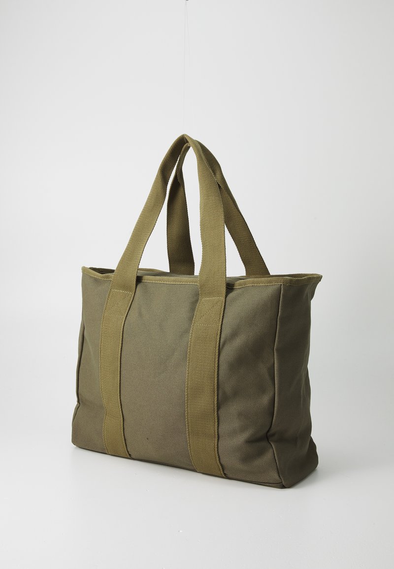 Zielona torba płócienna na ramię z dwiema mocnymi tkaninowymi uchwytami, prostokątny kształt i widoczne detale zszycia. Płaskie dno zapewniające stabilność.