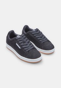 Dark gray suede sneakers with a low profile, featuring flat navy laces, a white midsole, and a gum rubber outsole. Simple branding present.