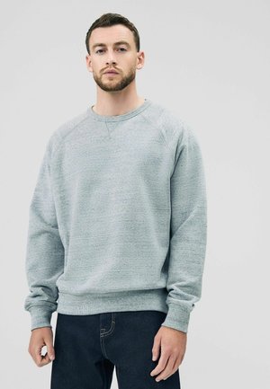 Grå fleece sweatshirt med tekstureret finish, raglanærmer og ribbede manchetter og kant. Bæres med mørke denimjeans.