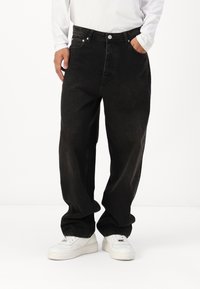 Black denim jeans with a loose fit, high waist, and front pockets. Worn with white sneakers for contrast. Textured fabric finish.
