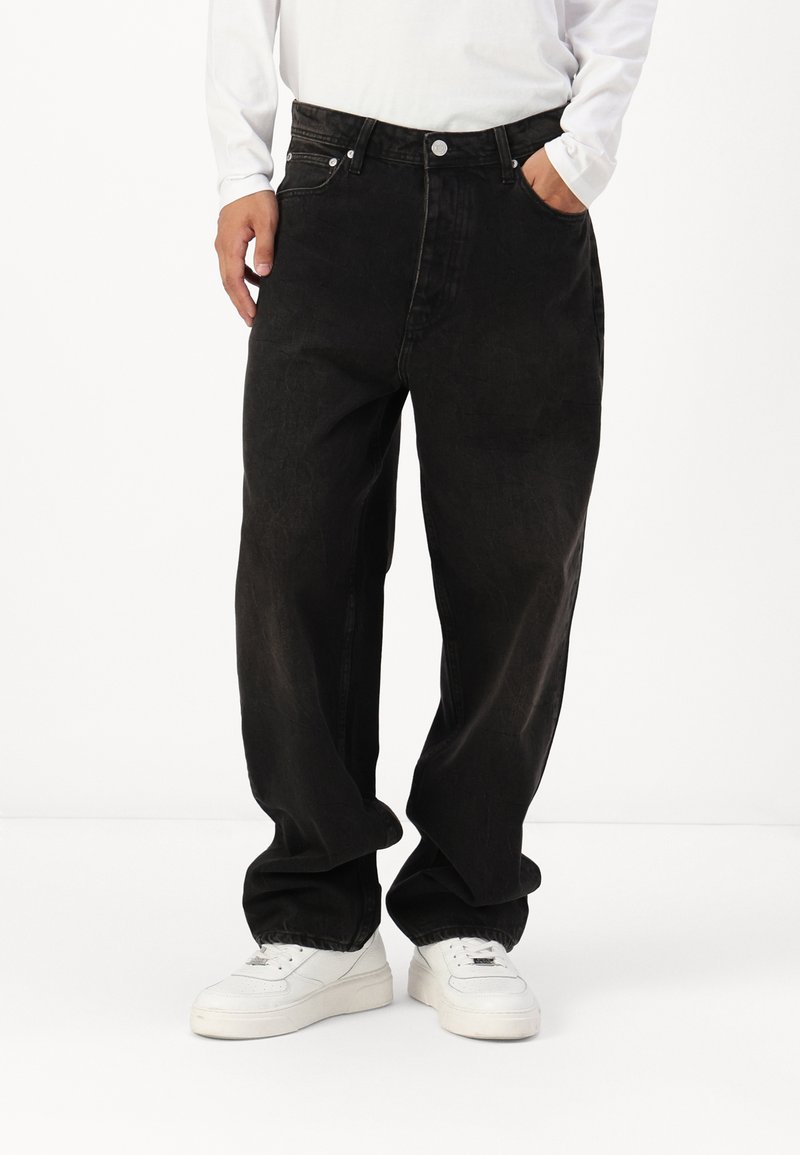 Jean en denim noir avec une coupe ample, taille haute et poches avant. Portés avec des baskets blanches pour le contraste. Finition en tissu texturé.
