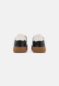 Black leather sneakers with white heel accents and a gum sole. Features embossed brand logo and contrasting stitching on the upper.