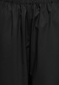 Tissu noir avec une ceinture élastique froncée et de légères plis verticaux, montrant une texture lisse et une finition mate.