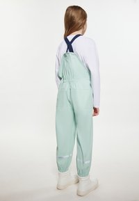 Vaikas vilki šviesiai žalias vandeniui atsparias kelnes su elastingais rankogaliais ir atšvaitinėmis juostelėmis, derindamas su balta ilgomis rankovėmis marškinėliais ir baltais aukštakulniais sportbačiais.