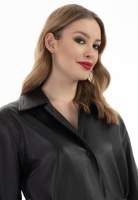 Camicia giacca in pelle nera con colletto, chiusura a pulsante e superficie liscia. Design semplice con una vestibilità rilassata.